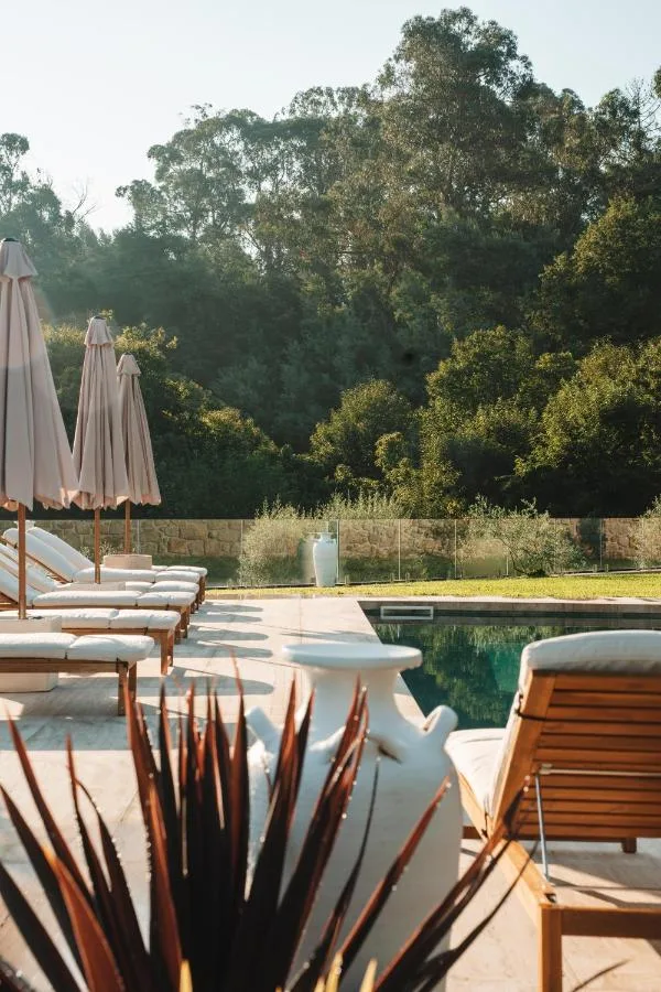 Piscina partilhada do Rosal Country Village ao nascer do sol — espreguiçadeiras, chapéus de sol em linho cru e vegetação atlântica